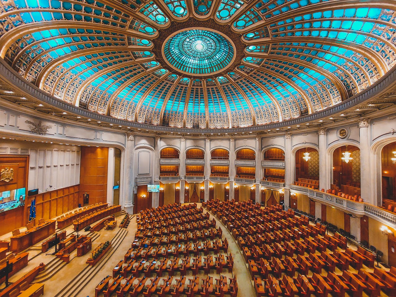 about-img Vibrant interior of a parliament hall with a grand dome and intricate architecture.