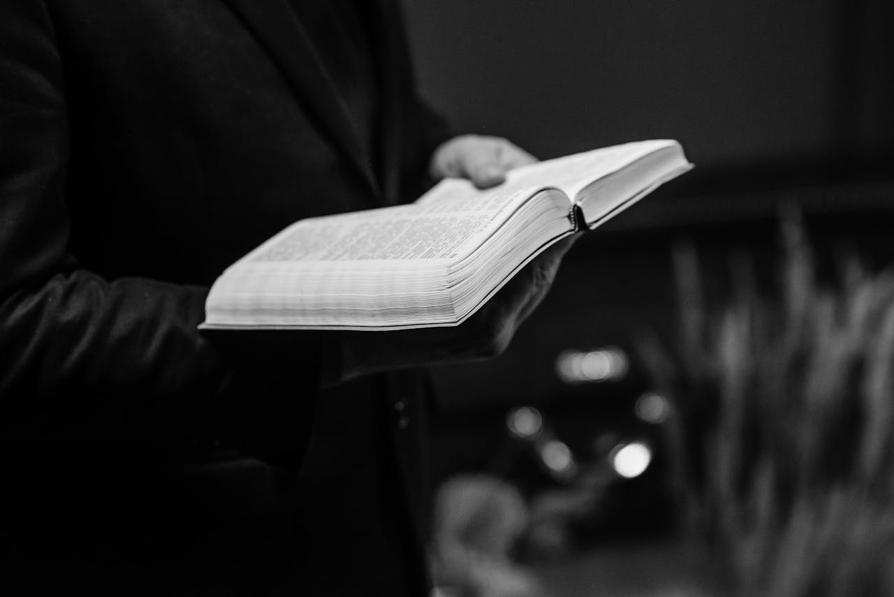 our-experience Grayscale close-up of a person holding an open Bible, conveying a sense of faith.